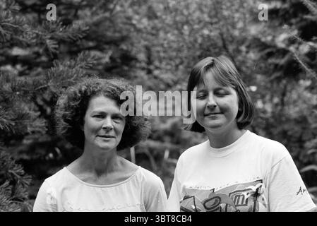 Due signore di Amnesty International, Whizgle News, Dutch Desk, Paesi Bassi, 1950 - 2000 il 14-08-1991. Questi sono gli elementi dell'immagine. In un ambiente naturale all'aperto, due donne stanno vicine, circondate da una vegetazione lussureggiante. Il fogliame appare ricco e denso, suggerendo un'atmosfera selvaggia. Lo sfondo presenta varie sfumature di verde e sfumature di forme morbide e sfocate, suggerendo alberi e piante. Entrambi gli individui presentano un comportamento calmo. Una donna ha capelli voluminosi e ricci che incornicia il viso, mentre la sua espressione trasmette un senso di portamento e contemplazione. Lei è wearin Foto Stock