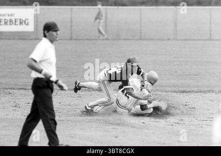 Pioniers -PSV Baseball, Whizgle News, Dutch Desk, Paesi Bassi, 1950 - 2000 on 29-08-1987. Questi sono gli argomenti nell'immagine. La scena cattura un momento dinamico su un campo da baseball, dove l'intensità del gioco è palpabile. In primo piano, due giocatori affrontano uno scontro ravvicinato; uno sta scivolando in una base, lanciando una nuvola di terra mentre si allunga per raggiungere in sicurezza. La sua uniforme è prevalentemente bianca con alcuni accenti colorati, il che potrebbe indicare la sua affiliazione alla squadra, e il suo casco è leggermente inclinato quando colpisce il terreno. L'altro giocatore, posizionato sopra di lui, indossa un Foto Stock