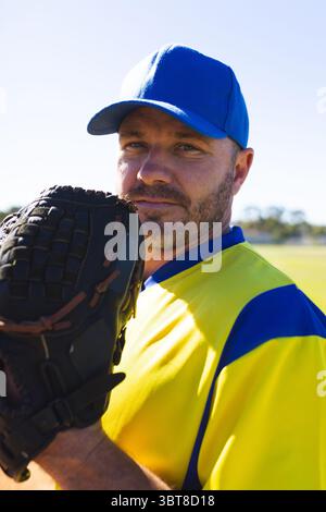 Uomo anziano in piedi sul campo da baseball con guanto in pelle con maglia gialla e berretto blu Foto Stock