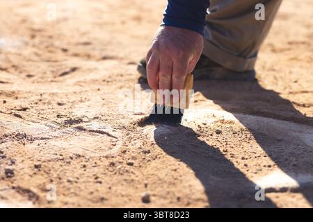 Senior man che usa una spazzola di legno che spazza lo sporco dalla linea del gesso sul campo da baseball, copia lo spazio Foto Stock
