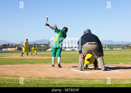 Giocatore di baseball maschile medio in uniforme verde che oscilla in una mazza di legno sul piatto di casa con baseball Foto Stock