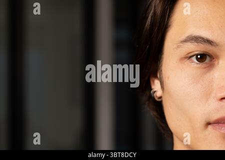 Uomo asiatico che mostra un piccolo orecchino a cerchio da vicino in camera con sfondo persiane, spazio copia Foto Stock
