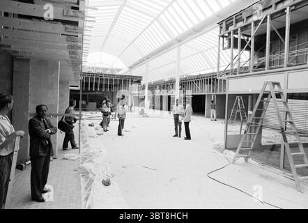 Nuovo centro commerciale Hoofddorp Shops and Kiosks Hoofddorp The Netherlands, Whizgle News, Dutch Desk, Paesi Bassi, 1950 - 2000 il 16-06-1988. L'immagine mostra questi argomenti. La scena cattura un cantiere spazioso caratterizzato da un ampio interno illuminato da un filtro luminoso e diffuso attraverso un tetto in vetro. Lo spazio architettonico è ancora in fase di sviluppo, con un mix di materie prime e attività di costruzione in corso evidenti ovunque. Sul lato sinistro, un gruppo di individui è riunito, con alcuni in piedi contro un muro e altri impegnati in conversazione. Foto Stock
