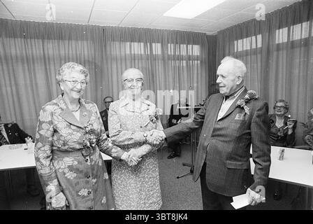 Premiate 2 donne per 25 anni. assistenza agli anziani. Awards, Whizgle News, Dutch Desk, Paesi Bassi, 1950 - 2000 il 02-10-1975. Questi sono gli elementi dell'immagine. La scena presenta un raduno al chiuso in cui tre anziani sono in prima linea. Una donna sulla sinistra indossa un abito a motivi geometrici dai colori vivaci, tra cui sfumature di blu, rosa e giallo. I suoi occhiali si siedono bassi sul naso e trasuda calore con un ampio sorriso. Accanto a lei c'è un'altra donna in un abito con motivi simili, anche se il suo vestito ha tonalità più morbide e disegni floreali. Indossa anche occhiali e condivide un esultante spettacolo Foto Stock