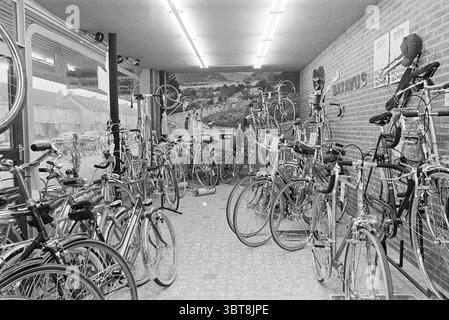 Negozio di biciclette interno Koning Beverwijk percorsi biciclette interni, Whizgle News, Dutch Desk, Paesi Bassi, 1950 - 2000 il 18-11-1976. Questi argomenti sono mostrati nell'immagine. La scena presenta un vivace negozio di biciclette pieno di una vasta gamma di biciclette. Gli interni sono caratterizzati da un mix di diversi modelli di bici, dalle biciclette da corsa con telai sottili alle mountain bike più robuste, tutte appoggiate su piedistalli o appoggiate contro le pareti. I colori delle biciclette spaziano dai rossi e blu luminosi alle tonalità metallizzate, creando una vivace tavolozza sullo sfondo di una parete di mattoni. Lo spazio è ben illuminato con fluoro Foto Stock