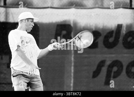 Tennis Brederode v.d. Mountain, Whizgle News, Dutch Desk, Paesi Bassi, 1950 - 2000 il 12-07-1995. Questi sono gli elementi dell'immagine. In una dinamica scena sportiva, un tennista maschile viene catturato a metà corsa mentre si prepara a colpire la palla. Indossa una T-shirt bianca dalla vestibilità morbida, decorata da un design grafico colorato, che contrasta piacevolmente con i suoi pantaloncini più scuri e leggermente sbiaditi. Gli shorts sono corti con stile e aggiungono un tocco di energia all'azione. Il giocatore ha un'espressione focalizzata, che indica concentrazione e determinazione. La sua posizione è atletica, con un piede in posizione Foto Stock