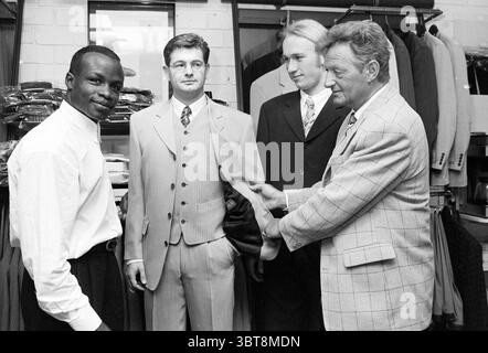 Presentazione della linea di abbigliamento Regilio Tuur (a sinistra nella foto), Whizgle News, Dutch Desk, Paesi Bassi, 1950 - 2000 il 02-05-1997. L'immagine include questi argomenti. La scena cattura un negozio di abbigliamento elegante, illuminato da un mix di luce soffusa e soffusa, creando un'atmosfera calda e al tempo stesso concentrata. Lo sfondo consiste in abiti ben disposti in vari colori e motivi, prevalentemente grigi, neri e sfumature sfumate, che riflettono un'estetica professionale. In primo piano, quattro individui sono impegnati in un'interazione dinamica. Una persona sta a sinistra, indossando una camicia bianca Foto Stock