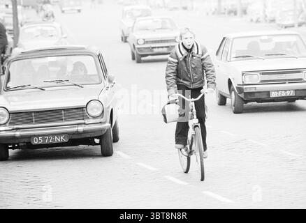 Ciclisti oppressi nel centro della città di Haarlem ciclisti ciclisti, Whizgle News, Dutch Desk, Paesi Bassi, 1950 - 2000 il 15-02-1978. L'immagine include questi argomenti. La scena cattura una strada movimentata di un'epoca passata, resa prevalentemente in tonalità di bianco e nero, che evoca un'atmosfera nostalgica. In primo piano, un giovane guida una bicicletta, la sua postura è leggermente scossa mentre percorre la strada. Indossa una giacca pesante, il che suggerisce un clima fresco, probabilmente indicante l'autunno o l'inizio della primavera. La sua espressione è concentrata, forse un mix di concentrazione e divertimento Foto Stock