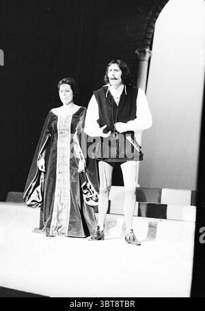 Opera: Il Pirata Bellini Opera operetta, Whizgle News, Dutch Desk, Paesi Bassi, 1950 - 2000 il 09-11-1977. Questi sono gli elementi dell'immagine. La scena cattura uno spettacolo teatrale ambientato su un palco con uno sfondo semplice ma sorprendente. Da un lato, una figura femminile è vestita con un abito elaborato, caratterizzato da maniche lunghe e un tessuto ricco che drappa elegantemente al suolo. L'abito presenta un pannello centrale di primo piano con colori contrastanti che ne esaltano l'aspetto reale. I suoi capelli sono modellati in modo classico e morbido, incorniciando il suo viso e conferendo un'aria di raffinatezza. Accanto a h Foto Stock