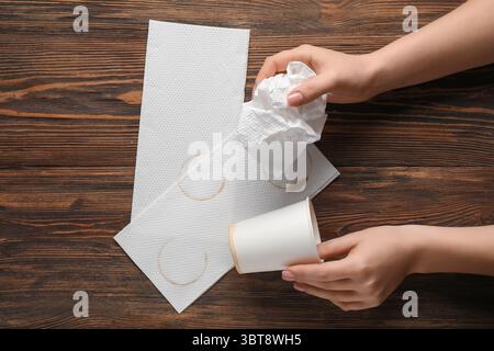 Mano femminile con tazza di carta, tovaglioli e macchie di caffè su sfondo in legno Foto Stock