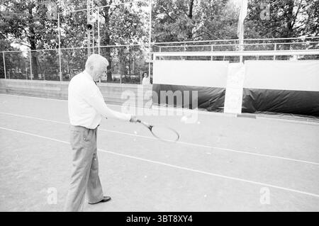 Apertura del campo di calcio Schoten VV Schoten Onze Gezellen Renova, Whizgle News, Dutch Desk, Paesi Bassi, 1950 - 2000 il 04-06-1988. L'immagine mostra questi argomenti. La scena mostra un campo da tennis, caratterizzato dalla sua superficie sabbiosa e leggermente usurata, suggerendo un utilizzo nel tempo. In primo piano, un uomo anziano è pronto ad agire, preparandosi a colpire una palla da tennis. È vestito con un abbigliamento dai colori chiari, che contrasta con i toni più caldi della corte e dell'ambiente circostante. I capelli dell'uomo sono grigi, e la sua postura riflette concentrazione e sicurezza, con la sua racchetta da tennis Foto Stock