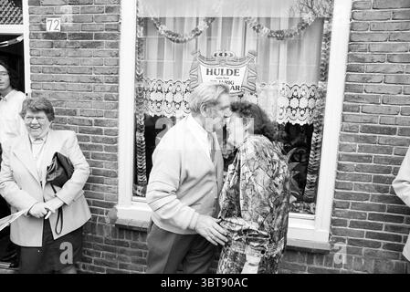 50 anni Kleijen@orst, Whizgle News, Dutch Desk, Paesi Bassi, 1950 - 2000 il 24-03-1992. Questi sono gli elementi dell'immagine. In un ambiente urbano vivace, una coppia si trova in prima linea, impegnata in un momento intimo, condividendo un bacio gioioso. L'uomo, vestito con un cardigan di colore chiaro e pantaloni scuri, ha una calda espressione, mentre la donna accanto a lui, con un vestito colorato e fantasia, irradia con gioia. C'è un'energia giocosa nella loro interazione, che suggerisce una festa o un'occasione speciale. Dietro di loro, un gruppo di spettatori aumenta la vivacità della scena. A sinistra, una donna Foto Stock