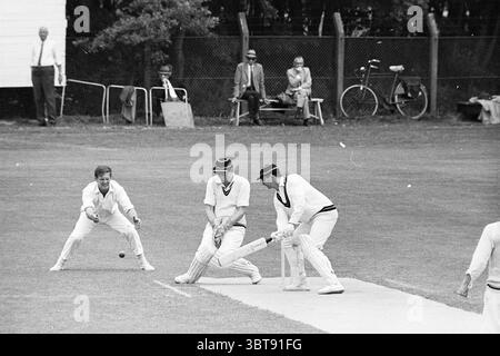 Red and White - H.C.C. Cricket, Whizgle News, Dutch Desk, Paesi Bassi, 1950 - 2000 il 16-06-1968. Questi argomenti sono mostrati nell'immagine. In un campo verde vivace, una partita di cricket si svolge sotto un cielo leggermente coperto, proiettando una luce soffusa sulla scena. I giocatori sono vestiti con un classico abbigliamento bianco da cricket, caratterizzato da pantaloni lunghi e maglioni coordinati. Un giocatore sta in piedi alla piega, con una mazza, gli occhi concentrati sulla palla che gli si avvicina. Indossa un cappello da cricket nero. Al suo fianco, un altro giocatore accovacciato in basso, pronto a prendere se necessario. La sua concentrazione è Foto Stock