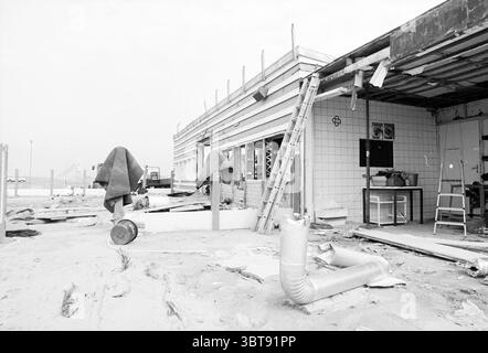 Demolizione di padiglioni IJmuiden Beach IJmuiden Paesi Bassi, Whizgle News, Dutch Desk, Paesi Bassi, 1950 - 2000 il 09-09-1993. Questi argomenti vengono visualizzati nell'immagine. La scena raffigura una struttura intemprata, parzialmente costruita, rivelando segni di abbandono e abbandono. Da un lato, c'è una struttura in legno che è stata lasciata esposta, che denota i resti scheletrici di un edificio. Le pareti sono rivestite con tavole di legno dipinte in sfumature tenui, mescolando grigi pallidi e bianchi che evocano un senso di desolazione. Sparpagliati in primo piano ci sono vari oggetti che suggeriscono partenze affrettate: Foto Stock