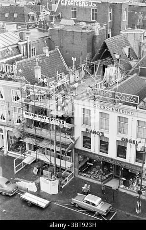Hotel Spaan Renovation Hotels, Whizgle News, Dutch Desk, Paesi Bassi, 1950 - 2000 on 27-03-1961. Questi argomenti vengono visualizzati nell'immagine. La scena cattura un vivace ambiente urbano durante un periodo di costruzione. In primo piano, un edificio a più piani è parzialmente coperto da impalcature, indicando i lavori di ristrutturazione in corso. I lavoratori edili possono essere visti manovrare intorno al sito, i loro movimenti intensi e laboriosi, suggerendo un'atmosfera vivace piena di attività. Sulla sinistra, la struttura presenta un ristorante con una luminosa segnaletica che suggerisce le sue offerte culinarie. Sotto, Foto Stock