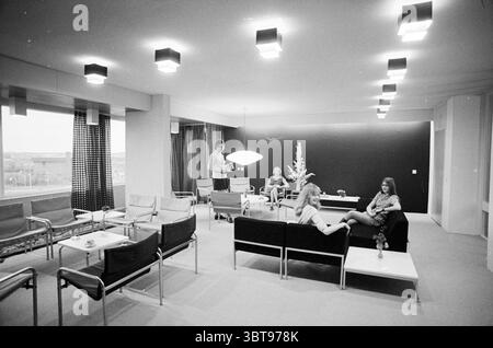 INTR. Huis ter Wijck Interior, Whizgle News, Dutch Desk, Paesi Bassi, 1950 - 2000 il 18-11-1971. L'immagine contiene questi argomenti. La scena raffigura un interno moderno e minimalista, caratterizzato da una spaziosa area lounge con un ambiente sofisticato e un po' retrò. La sala è illuminata da una serie di plafoniere rettangolari che emettono una luce soffusa e diffusa, creando un'atmosfera calda ma discreta. Nel centro, diversi gruppi di persone sono organizzati casualmente. Un uomo sta vicino a una finestra, impegnato in una conversazione, mentre due donne sono sedute su un elegante divano nero. Una donna si appella Foto Stock