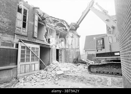 Demolizione Bolleschuur Lisse demolizione demolizione cantieri Lisse, Whizgle News, Dutch Desk, Paesi Bassi, 1950 - 2000 il 05-03-1990. L'immagine mostra questi argomenti. La scena raffigura un paesaggio urbano grintoso sotto cieli grigi e ricoperti, contribuendo a creare un umore cupo. Un grande veicolo da costruzione, con un robusto braccio dotato di un artiglio, domina un lato dell'ambientazione, attivamente impegnato nella demolizione di un edificio fatiscente. Il telaio in metallo dell'auto risplende, contrastando con i colori tenui dell'ambiente circostante. L'edificio che viene demolito ha sezioni che si stanno sgretolando, smascherando Foto Stock