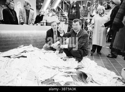 Disegna lotti presso il negozio di abbigliamento De Lords Heemstede Miscellaneous Lottery Heemstede Paesi Bassi, Whizgle News, Dutch Desk, Paesi Bassi, 1950 - 2000 il 14-11-1988. L'immagine contiene questi argomenti. In un vivace ambiente retail, una scena disordinata si sviluppa su un pavimento piastrellato dove fuoriesce una grande pila di carta, ad esempio ricevute o materiali promozionali, creando un netto contrasto con le piastrelle grigie lucide. Due uomini si inginocchiano accanto al cumulo, uno gestante animato con un sorriso, l'altro sfoggia un'espressione sfarzosa, entrambi vestiti con abiti che suggeriscono un look casual ma professionale Foto Stock