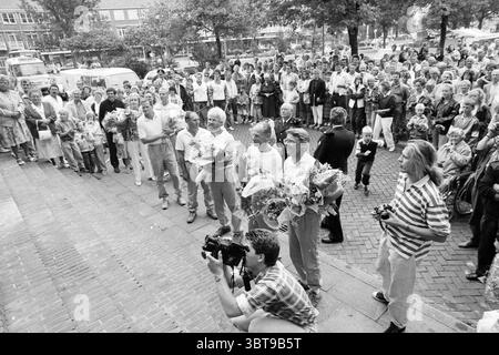 Tour a piedi della Croce Rossa arrivo a piedi, Whizgle News, Banco olandese, Paesi Bassi, 1950 - 2000 il 10-09-1988. Questi sono gli elementi dell'immagine. In una vivace scena all'aperto, una grande folla si è riunita, riempiendo una strada acciottolata che sembra vivace con entusiasmo e attesa. Le persone sono un mix di età, con alcuni in piedi in gruppi e altri seduti o appoggiati a veicoli e strutture vicini. In primo piano ci sono diversi individui che tengono mazzi di fiori, le loro espressioni suggeriscono che stanno celebrando o onorando qualcuno. I fiori aggiungono spruzzi di colore Foto Stock