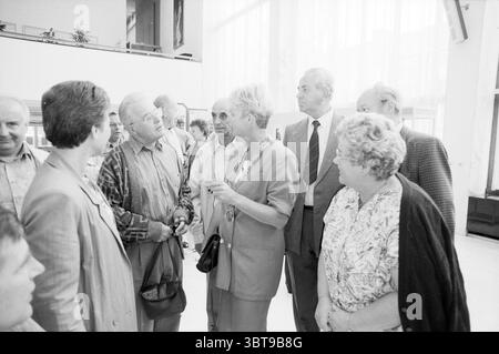 Reception tedeschi IJmuiden municipio IJmuiden Paesi Bassi, Whizgle News, Dutch Desk, Paesi Bassi, 1950 - 2000 il 05-09-1991. L'immagine mostra questi argomenti. La scena raffigura un gruppo di persone impegnate nella conversazione, probabilmente in un ambiente interno spazioso caratterizzato da alti soffitti e grandi finestre che consentono l'ingresso di un'ampia luce naturale. I colori sono prevalentemente attenuati, con sfumature di grigio e toni delicati, che suggeriscono un'atmosfera cupa ma elegante. In primo piano, un gruppo eterogeneo di individui è raggruppato insieme. Sono vestiti con abiti formali o semi-formali, r Foto Stock