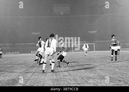AJAX - Napoli Football Ajax, Whizgle News, Dutch Desk, Paesi Bassi, 1950 - 2000 il 21-01-1970. L'immagine contiene questi argomenti. La scena cattura una vivace partita di calcio, ambientata in un ampio stadio all'aperto. Il campo è coperto da uno strato di ghiaccio o neve, evidenziando le condizioni in cui i giocatori competono. In primo piano, diversi giocatori sono coinvolti dinamicamente, mostrando una serie di movimenti atletici. Un giocatore, che indossa una maglia a strisce con il numero 9, si distingue su uno sfondo più scuro, la sua postura suggerisce sia un tentativo di ottenere il controllo della palla Foto Stock