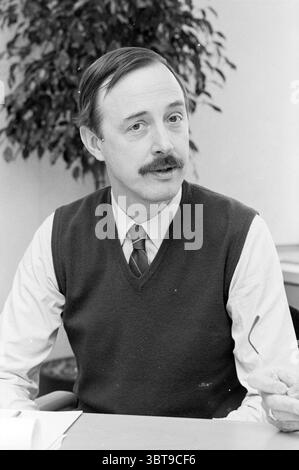 Ritratto di un membro del COR Haarlem Haarlem Paesi Bassi, Whizgle News, Dutch Desk, Paesi Bassi, 1950 - 2000 il 08-01-1985. Questi sono gli argomenti nell'immagine. Un uomo con baffi ben curati e capelli scuri e corti è seduto a un tavolo, mostrando un atteggiamento amichevole. È vestito con una camicia color crema, con un gilet scuro che contrasta delicatamente con il tessuto più leggero. L'ambiente è uno spazio ufficio, suggerito dall'elegante tavolo e da una pianta verde in vaso sullo sfondo, che aggiunge un tocco di calore all'ambiente. L'umore generale è professionale ma allo stesso tempo adeguato Foto Stock