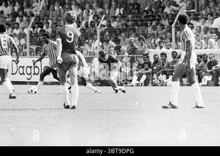 Haarlem - Robin Hood Football Haarlem, Whizgle News, Dutch Desk, Paesi Bassi, 1950 - 2000 il 15-08-1976. Questi argomenti vengono visualizzati nell'immagine. La scena è ambientata su un campo verde vivace, pieno di energia da una partita di calcio in pieno svolgimento. La superficie erbosa è ben mantenuta, in netto contrasto con le tonalità del bianco e nero che dominano la scena, conferendole un aspetto classico. In primo piano, un giocatore con una maglia scura è concentrato con attenzione, piegandosi in basso mentre manovra abilmente la palla. La sua postura riflette la determinazione, con una gamba allungata in avanti e l'altra pronta a ruotare. Surrou Foto Stock