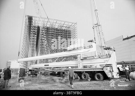 Lavori di sollevamento Yamaha Schiphol-Rijk Schiphol-Rijk, Whizgle News, Dutch Desk, Paesi Bassi, 1950 - 2000 il 24-02-1992. Questi argomenti vengono visualizzati nell'immagine. La scena raffigura un cantiere industriale, caratterizzato da un'alta struttura scheletrica che suggerisce la struttura di un grande edificio in fase di costruzione. La struttura è estesa, con travi metalliche e impalcature disposte in un modello simile a una griglia, che si innalza verso il cielo. In primo piano, una grande gru domina la composizione e il suo braccio si estende verso il cantiere, contribuendo al senso di scala e attività. Il Foto Stock