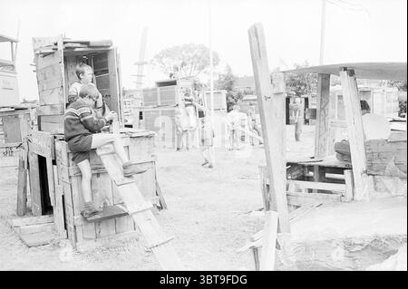Città dei ragazzi Beverwijk Giochi festivi vacanze vacanze vacanze campo, Whizgle News, Dutch Desk, Paesi Bassi, 1950 - 2000 il 18-07-1968. Questi sono gli elementi dell'immagine. Nella scena, un gruppo di bambini è impegnato in attività ludiche in un ambiente esterno improvvisato pieno di strutture in legno. Le strutture, apparentemente realizzate con casse e tavole, possiedono un fascino rustico. Alcuni bambini sono attivamente arrampicati, mentre altri sono seduti sui gradini di legno o all'interno delle costruzioni, mostrando la loro creatività ed energia. La tavolozza dei colori è prevalentemente silenziata e monocromatica, em Foto Stock