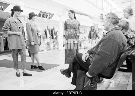 Sfilata di moda di Brokx Mode, Whizgle News, Dutch Desk, Paesi Bassi, 1950 - 2000 il 08-03-1995. L'immagine include questi argomenti. Nella scena, un vivace centro commerciale al coperto funge da sfondo. La luce naturale inonda lo spazio, con un'illuminazione soffusa che esalta i colori vibranti degli abiti esposti nei negozi intorno. Tre manichini sono in piedi con sicurezza in una disposizione impressionante. Ogni abito è unico e sfoggia stili diversi, uno sfoggia un blazer grigio sartoriale e pantaloni a righe, che trasudano un'atmosfera chic e moderna. Un altro manichino indossa un outfit più rilassato con un look morbido e pacato Foto Stock