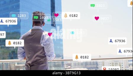 Uomo in piedi in gilet e camicia con vista sullo skyline dal balcone, con icone di notifica fluttuanti Foto Stock