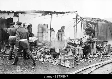 Incendio al mercato ortofrutticolo che ha distrutto due magazzini Boon Company e Steensma Branden Fire Brigade Haarlem Koudenhorn Paesi Bassi, Whizgle News, Dutch Desk, Paesi Bassi, 1950 - 2000 il 01-03-1963. Questi sono gli argomenti nell'immagine. La scena raffigura una situazione caotica e intensa, caratterizzata da una prevalenza di fumo che si intreccia con la luce soffusa dell'ambientazione. In primo piano, diverse figure in divise oscure sono attivamente coinvolte nelle conseguenze di un disastro. I vigili del fuoco, rivestiti di attrezzatura protettiva, sono visibili e i loro volti mostrano determinazione come Foto Stock