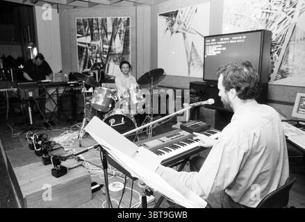 The Attack Haarlem Jazz Club, Whizgle News, Dutch Desk, Paesi Bassi, 1950 - 2000 il 26-04-1991. Questi argomenti sono mostrati nell'immagine. In una stanza poco illuminata e piena di atmosfera, due musicisti si esibiscono in un'esibizione accattivante. Lo spazio appare intimo, con le pareti adornate con grandi opere d'arte astratte che aggiungono un tocco moderno all'atmosfera. Verso l'avanguardia, un musicista si siede a una tastiera e la sua concentrazione è intensa mentre suona. Ha i capelli di media lunghezza e indossa una camicia aderente, appoggiandosi leggermente verso un microfono posizionato vicino al suo viso, suggerendo una p vocale impegnata Foto Stock