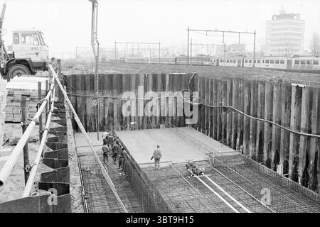 Cantiere stazione VAM cantieri edili, Whizgle News, Dutch Desk, Paesi Bassi, 1950 - 2000 al 27-04-1978. Questi argomenti sono mostrati nell'immagine. La scena raffigura un cantiere caratterizzato da un alto e profondo scavo circondato da alte tavole di legno che sostengono saldamente la terra. Nella parte inferiore della fossa è in corso la preparazione di una lastra di cemento parzialmente armato, con tondino in acciaio che sporge visibilmente dalla superficie, a indicare che è in attesa di ulteriori lavori di costruzione. In primo piano, diversi lavoratori sono impegnati nei loro compiti, vestiti con attrezzature di sicurezza, incluso Foto Stock