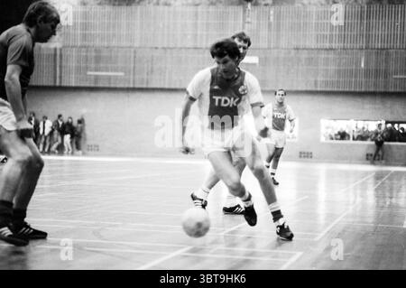 Old Ajax - Scandals Indoor football, Whizgle News, Dutch Desk, Paesi Bassi, 1950 - 2000 il 02-01-1988. Questi sono gli argomenti nell'immagine. La scena cattura una partita di calcio al coperto in una spaziosa palestra. Il pavimento è in legno lucido, che riflette l'illuminazione superiore, che proietta un bagliore luminoso sull'azione. Tre giocatori sono impegnati in un momento intenso, con i loro volti che mostrano concentrazione e determinazione. Due giocatori sulla sinistra indossano uniformi scure abbinate, mentre il giocatore al centro si distingue con una maglia bianca adornata con le lettere "TDK". Anche i suoi pantaloncini sono bianchi, truffatore Foto Stock