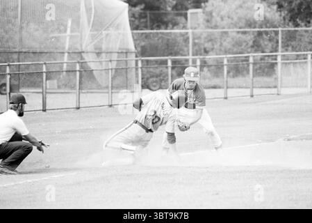 Baseball Nicols-Sparta Baseball, Whizgle News, Dutch Desk, Paesi Bassi, 1950 - 2000 il 27-07-1979. Questi sono gli elementi dell'immagine. In una dinamica scena di baseball, due giocatori sono impegnati in un momento di intensa competizione su un campo erboso. Il giocatore che scorre verso la base, indossando una maglia e un berretto, viene catturato durante l'azione, mentre lo sporco viene calpestato intorno a lui, contribuendo al senso di movimento e urgenza. La sua uniforme è contrassegnata da numeri e lettere che mostrano l'affiliazione della sua squadra. Avversario, il giocatore difensivo, vestito con una maglia a contrasto, accovacciato per essere pronto a combattere Foto Stock