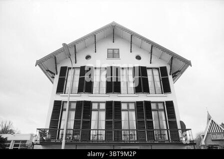 Est. H'str 252 Santpoort Santpoort-Noord Hoofdstraat, Whizgle News, Dutch Desk, Paesi Bassi, 1950 - 2000 il 20-03-1992. L'immagine include questi argomenti. La scena rivela una struttura architettonica suggestiva, caratterizzata dal suo design simmetrico e dalle caratteristiche prominenti. L'edificio presenta una distinta linea triangolare del tetto, accentuata da grondaie decorative che si estendono verso l'esterno. Una serie di alte e strette finestre dominano la facciata, incorniciata da persiane scure che sono ben chiuse, in contrasto con la facciata bianca della casa. La parte superiore della struttura comprende una finestra circolare centrale, Foto Stock