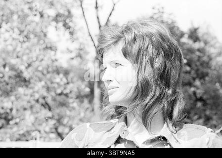 Models Loe-Loe Models, Whizgle News, Dutch Desk, Paesi Bassi, 1950 - 2000 il 29-05-1971. L'immagine include questi argomenti. La scena presenta una donna con capelli lunghi e fluenti, disegnati con onde morbide, che creano un senso di movimento. Il suo profilo è ben visibile, e guarda di lato, suggerendo un momento di contemplazione o riflessione. L'espressione facciale cattura un umore sereno ma pensivo, con sottili riflessi che sottolineano il suo zigomo e la curva della sua mascella. Lo sfondo include una vegetazione sfocata, che indica un ambiente lussureggiante pieno di alberi e fogliame. L'interazione di Foto Stock