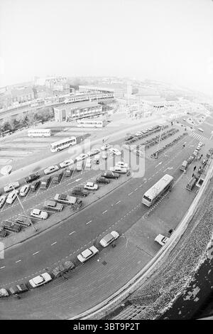 Report NZH Leiden Noord Zuid Hollandse Vervoersmaatschappij N.V. NZ, Whizgle News, Dutch Desk, Paesi Bassi, 1950 - 2000 il 25-11-1970. Questi sono gli elementi dell'immagine. La scena presenta un'ambientazione urbana estesa vista da un alto punto panoramico. La strada è un'ampia strada semicircolare costeggiata da una varietà di veicoli, tra cui auto e autobus, parcheggiati sia longitudinalmente che ad angoli, rivelando un mix di colori come bianco, grigio e toni tenui. Alcuni veicoli sembrano in attesa di passeggeri o cambiare turno, mentre altri sembrano inattivi. L'architettura circostante e' caratterizzata da un'architettura Foto Stock