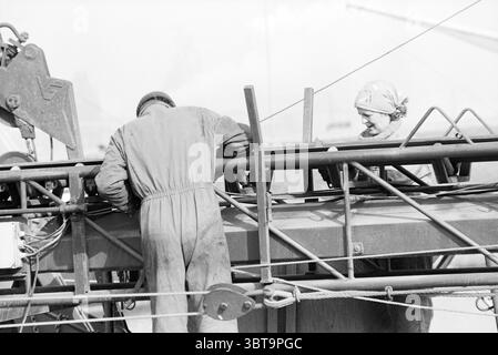 Altiforni in autobus (stazione degli autobus), Whizgle News, Dutch Desk, Paesi Bassi, 1950 - 2000 il 09-03-1993. Questi argomenti vengono visualizzati nell'immagine. La scena cattura un momento di laborioso impegno in un ambiente che ricorda un porto affollato o un cantiere edile. Due individui sono presenti in modo prominente, coinvolti nei loro compiti. Uno, vestito con una tuta scura, si appoggia leggermente su una struttura metallica, apparentemente per ispezionare o manipolare una macchina. La postura della figura suggerisce la concentrazione, con la concentrazione verso il basso. Il secondo individuo, posizionato vicino al macchinario, ha una testa luminosa Foto Stock