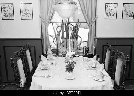 Interno del ristorante Wijcker Herberg Beverwijk Beverwijk Zeeweg Paesi Bassi, Whizgle News, Dutch Desk, Paesi Bassi, 1950 - 2000 al 27-08-1979. Questi sono gli argomenti nell'immagine. La scena raffigura un'intima area da pranzo che trasuda un'atmosfera calda e invitante. Un tavolo rotondo è elegantemente posizionato al centro, drappeggiato da una tovaglia bianca croccante che presenta delicati motivi floreali impressi sulla superficie. In cima al tavolo, un piccolo mazzo di fiori splendidamente disposti aggiunge un tocco di colore con delicate sfumature di rosa e giallo. Attorno al tavolo ci sono diverse sedie di legno ornamentali W. Foto Stock