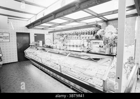 INTR. Butcher van 't Hoff en Zonen Interior, Whizgle News, Dutch Desk, Paesi Bassi, 1950 - 2000 il 01-10-1974. L'immagine include questi argomenti. La scena presenta un caratteristico spazio interno, probabilmente un panificio o una gastronomia, caratterizzato da un'atmosfera nostalgica e invitante. Il punto focale è una lunga vetrina, piena di una serie di torte, pasticcini e altri prodotti da forno, ognuna splendidamente disposta per mostrare i loro colori e le loro texture seducenti. La cassa in vetro riflette una delicata lucentezza, esaltando il fascino visivo delle prelibatezze all'interno, che vanno dai dolci dorati a quelli vivaci, Foto Stock