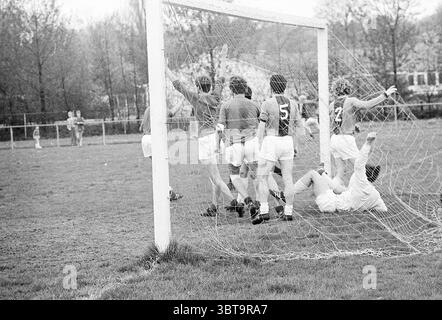 Van Nispen - Lisse Football, Whizgle News, Dutch Desk, Paesi Bassi, 1950 - 2000 il 10-05-1970. Questi argomenti sono mostrati nell'immagine. La scena raffigura un momento energico su un campo sportivo erboso, dove un piccolo gruppo di giocatori è impegnato in una partita di calcio. In primo piano, un portiere è a terra, apparentemente avendo appena perso un tiro in porta. Sembra frustrato, con le mani appoggiate sull'erba, mentre i suoi compagni di squadra mostrano reazioni diverse. A sinistra, due giocatori, che indossano maglie abbinate numerate 5 e 2, sono in posa celebrativa, alzando le braccia in trionfo. Nelle vicinanze, AN Foto Stock