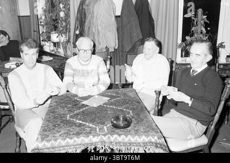 Bridge team foursomes Bridge, Whizgle News, Dutch Desk, Paesi Bassi, 1950 - 2000 il 14-03-1984. Questi argomenti vengono visualizzati nell'immagine. In un intimo e luminoso interno, quattro uomini sono seduti intorno ad un tavolo di legno scuro adornato con una tovaglia riccamente decorata. Il panno presenta un design centrale che contrasta con i colori tenui dell'ambiente, aumentando l'interesse visivo. Gli uomini, vestiti con un mix di abbigliamento casual e leggermente più formale, sono impegnati in un gioco di carte. Ognuno ha una mano di carte, le sue espressioni un mix di concentrazione e cameratismo. Un uomo, occhiali sportivi e una S di colore chiaro Foto Stock