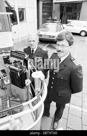 Comando dei vigili del fuoco trasferimento Haarlem, Whizgle News, Dutch Desk, Paesi Bassi, 1950 - 2000 nel 1990. L'immagine include questi argomenti. Nella scena, due uomini in uniforme sono prominenti in primo piano, ognuno mostrando un comportamento distintamente autorevole. Entrambi indossano divise scure e vestite ornate da insegne che suggeriscono il loro ruolo di ufficiali. L'uomo a sinistra, con i capelli argentati, ha un'espressione seria ed è leggermente orientato verso la fotocamera. Sembra impegnato e attento, suggerendo un momento di contemplazione o di discussione. Il secondo uomo, a destra, ha baffi e un bicchiere Foto Stock