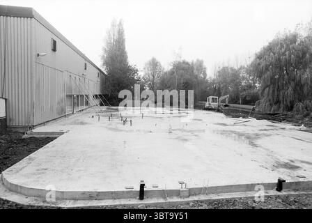 Fondazione di espansione della società Woodward Hoofddorp Paesi Bassi, Whizgle News, Dutch Desk, Paesi Bassi, 1950 - 2000 il 17-10-1990. Questi argomenti sono mostrati nell'immagine. La scena raffigura un cantiere, caratterizzato da un'atmosfera dura e industriale. In primo piano, una grande lastra di cemento piatta si estende lungo il terreno, sembrando liscia e non finita. La lastra è punteggiata da armature metalliche che si attaccano in vari punti, indicando la preparazione per futuri elementi di costruzione. A sinistra, con le sue nervature si erge una grande struttura metallica, probabilmente un magazzino o un edificio industriale Foto Stock