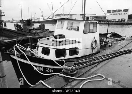 Barca da pesca inglese mn 26 porto Beverwijk pesca e altri pescivendoli pesca Beverwijk Paesi Bassi, Whizgle News, Dutch Desk, Paesi Bassi, 1950 - 2000 il 02-01-1987. Questi argomenti sono mostrati nell'immagine. La scena è ambientata in un porto, dove una piccola e robusta barca riposa al molo. L'imbarcazione, dipinta in tonalità profonde di bianco e nero, presenta una cabina compatta con tetto piatto. La cabina è dotata di più finestre, alcune con tende parzialmente disegnate, che lasciano intendere uno spazio abitabile. Un grande parafango è appeso sul lato, la sua forma rotonda contrasta con le linee rette della struttura dell'imbarcazione Foto Stock
