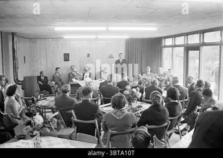 R.K. Clubhouse of the Playground Planetenlaan Opening Openings put into use, Whizgle News, Dutch Desk, Paesi Bassi, 1950 - 2000 il 03-11-1962. Questi sono gli argomenti nell'immagine. La scena si sviluppa in una sala accogliente caratterizzata da pannelli in legno che creano un'atmosfera calda e invitante. L'illuminazione è morbida e diffusa, emessa da apparecchi fluorescenti sopra, che emettono una luce soffusa in tutto lo spazio. In primo piano, un gruppo di persone sedute riempie la scena. Sono vestite in abiti formali, creando un senso di professionalità e decoro. Alcuni abiti sartoriali sono impreziositi da Foto Stock