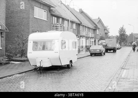 Caravan in Beverwijk Street Caravan camp Caravan Residents, Whizgle News, Dutch Desk, Paesi Bassi, 1950 - 2000 il 28-06-1978. L'immagine contiene questi argomenti. La scena presenta una strada tranquilla e urbana catturata con un'estetica monocromatica che le conferisce un'atmosfera vintage. Su un lato della strada, una serie di modeste case cittadine in mattoni fiancheggiano la strada. Le loro facciate mostrano una combinazione di toni tenui, che vanno principalmente dal grigio chiaro alle tonalità più scure, con tetti inclinati impreziositi da piastrelle marrone-rossastro. In primo piano, una carovana bianca affusolata è parcheggiata sul marciapiede, sta Foto Stock