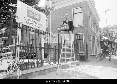 Direttore Tesselaar di 06-0013 il centro di emergenza in caso di guasto su una scala di fronte al suo edificio a Kennemerplein 2 Haarlem Kennemerplein Paesi Bassi, Whizgle News, Dutch Desk, Paesi Bassi, 1950 - 2000 il 17-05-1992. Questi argomenti sono mostrati nell'immagine. In questa scena, un uomo è seduto su una scala alta, arroccato su una struttura di legno. Indossa una tuta formale, che contrasta con l'ambiente informale. L'edificio dietro di lui è caratterizzato dalla sua facciata in mattoni rossi, caratterizzata da grandi finestre che riflettono l'ambiente urbano circostante. L'architettura ha un classico Foto Stock